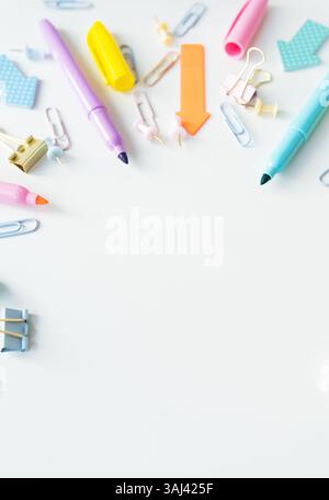 Pastellfarbene Schreibwaren wie Marker, Büroklammern und Stecknadeln sind auf weißem Hintergrund angeordnet und schaffen so ein fröhliches und organisiertes Werk Stockfoto