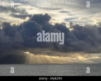 Sonnenstrahlen brechen durch schwere Sturmwolken über dem Ozean und werfen goldenes Licht über das Meer in einer dramatischen, stimmungsvollen Meereslandschaft. Stockfoto