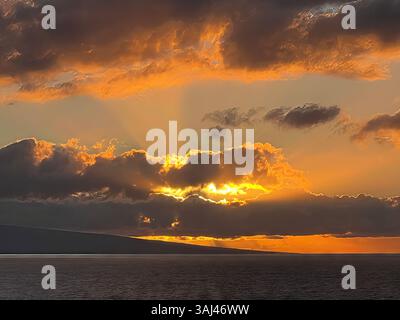 Sonnenuntergang über dem Ozean mit dramatischen Wolken und goldenen Strahlen, die durchbrechen und ein Leuchten über Meer und Himmel in einem atemberaubenden Moment der Küste werfen Stockfoto
