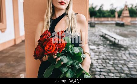 Eine Frau in einem schwarzen Kleid hält einen Strauß roter Rosen. Das Konzept von Romantik und Liebe, denn die Frau ist elegant gekleidet und die Rosen sind ein Symbiose Stockfoto