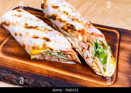 Zwei gegrillte Burritos sitzen auf einer Holzplatte, gefüllt mit buntem Gemüse, herzhaftem Fleisch und geschmolzenem Käse. Die warmen Tortillas weisen Zeichen auf Stockfoto
