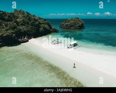 Atemberaubender Blick über die Drohne auf einen tropischen Strand auf den Philippinen mit türkisfarbenem Wasser, lebhaftem Grün und einem ruhigen Auslegerboot Stockfoto
