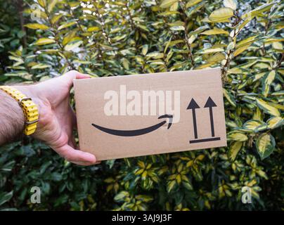 Paris, Frankreich - 7. Februar 2025: Ein Hand mit einer gelben Uhr hält ein kleines Papppaket, das mit einem Amazon Smile Logo und Orientierungspfeilen in f gekennzeichnet ist Stockfoto