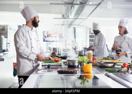 Verschiedene Köche schneiden mit einem Messer Gemüse und frisches Gemüse und bereiten Zutaten für ein neues Gourmetgericht in der Restaurantküche zu. Professionelle kulinarische Techniken für ein gehobenes kulinarisches Erlebnis. Stockfoto