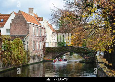 Ein Touristenboot, das die Peerdenbridge überquert, eine charmante kleine Brücke über den Groenerei-Kanal, eine der schönsten und grünsten Wasserstraßen Brügge. Stockfoto