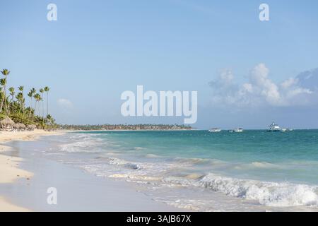 Palmen säumen den Sandstrand, während ruhige Wellen gegen den Strand plätschern. Mehrere Boote schweben im türkisfarbenen Wasser unter einem klaren blauen Himmel und bilden eine Erbse Stockfoto