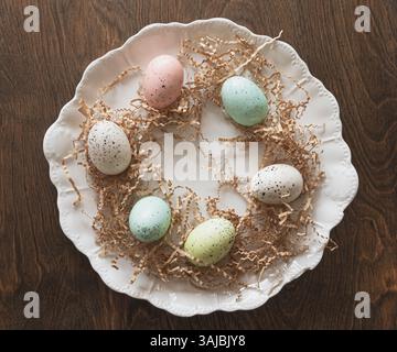 Weißer Porzellanteller mit pastellfarbenen gesprenkelten Eiern und braunem Knitterpapier Stockfoto