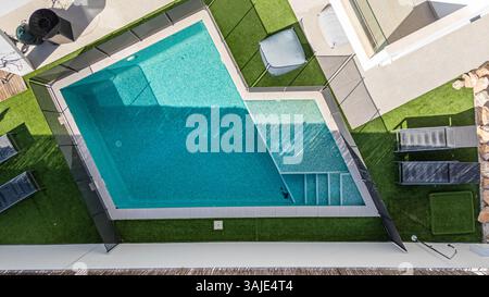Blick aus der Vogelperspektive auf einen kleinen privaten Pool mit Liegestühlen und Rasenbereich, umgeben von Zäunen. Stockfoto