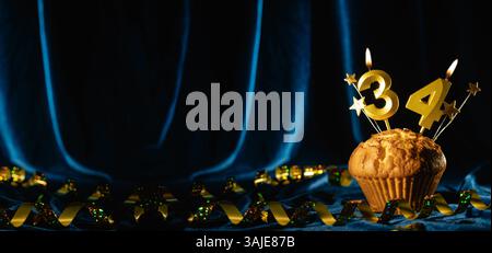 Nummer 34 goldene Festkerze und kleine Sterne in süßem Cupcake auf hellblauem Samthintergrund. Konzept der Feier von Geburtstag, Jubiläum Stockfoto