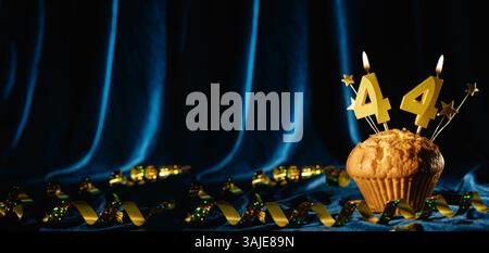 Nummer 44 goldene Festkerze und kleine Sterne in süßem Cupcake auf hellblauem Samthintergrund. Konzept der Feier von Geburtstag, Jubiläum Stockfoto