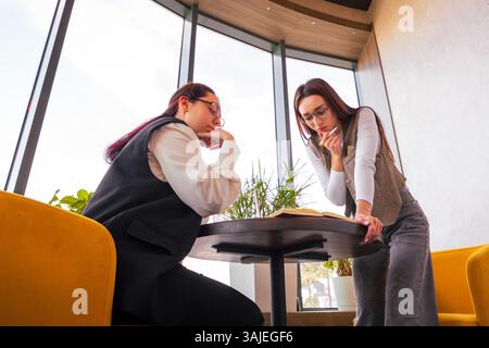 Ehrgeizige junge Geschäftsfrauen, die bei einer Tasse Kaffee an einem gemütlichen Kaffeetisch zusammenarbeiten. Besprechung von Marketingtaktiken. Konzept von Teamwork und Remote of Stockfoto