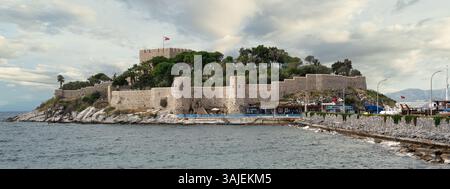 Das Schloss Kusadasi, das sich in der Provinz Aydin in der Türkei befindet, erhebt sich majestätisch auf einem Hügel, umgeben von grünem Grün und zerklüfteten Küsten. Wellen schlagen sanft gegen die Befestigungsanlagen Stockfoto