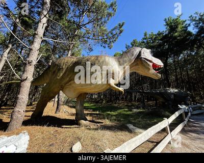 Eine Tyrannosaurus rex-Statue in Waldumgebung mit Bäumen und blauem Himmel. Stockfoto
