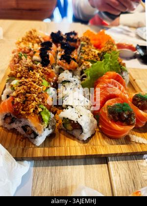 Verschiedene Sushi-Brötchen und Sashimi werden kunstvoll auf einem Holztablett in einem Restaurant präsentiert. Stockfoto