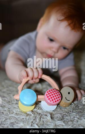 Rotes Haar Baby Mädchen krabbelt auf dem Boden und hält Babyspielzeug in der Hand Porträt zu Hause auf Teppich. Stockfoto