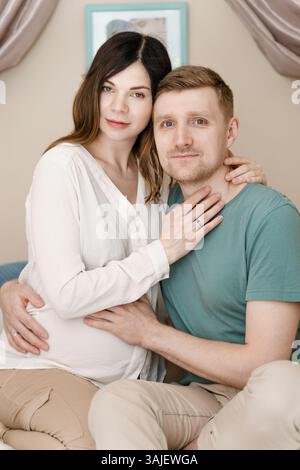 Glückliche schwangere Frau und Mann, die sich zu Hause umarmen Stockfoto