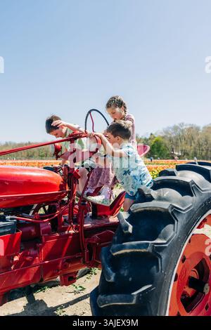Kinder klettern und spielen auf einem knallroten Vintage-Traktor Stockfoto