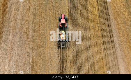 Traktor pflügt ein Feld von oben. Luftaufnahme eines roten Traktors, der auf trockenem Feld arbeitet, zeigt den landwirtschaftlichen Prozess des Pflügens und der Vorbereitung Stockfoto