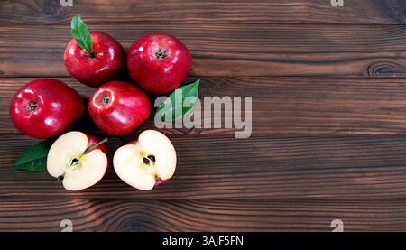 Frische rote Äpfel auf Holzoberfläche. Eine Nahaufnahme von fünf roten Äpfeln, die auf einer Holzoberfläche angeordnet sind, mit zwei Äpfeln, die halbiert werden, um ihre saftigen Äpfel zu enthüllen Stockfoto
