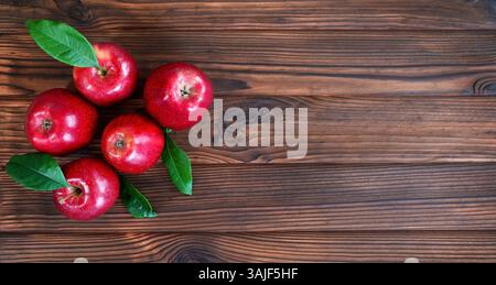 Rote Äpfel mit Blättern auf Holzoberfläche. Eine Aussicht von oben auf fünf glänzend rote Äpfel, die auf einer rustikalen Holzoberfläche angeordnet sind, mit grünen Blättern, die eine hinzufügen Stockfoto
