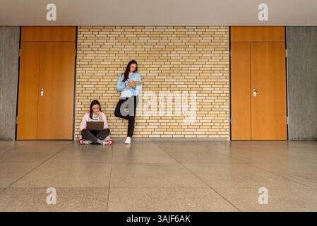 Zwei Studentinnen, die mit Laptop und Büchern in der Lobby der Universität studieren Stockfoto