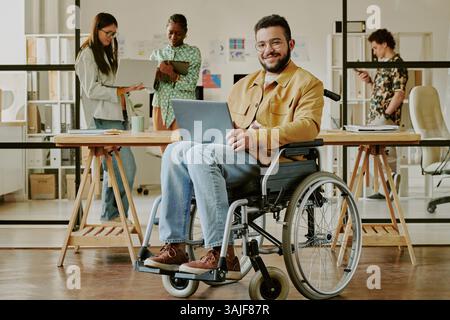 Programmiergerät für junge Erwachsene mit Laptop, der die Kamera anlächelt, während er im Büro für Porträts posiert Stockfoto