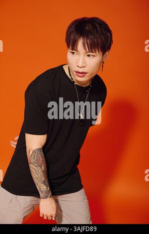 Ein stilvoller junger asiatischer Mann zeigt selbstbewusst seine Mode an einer leuchtend orangen Wand. Stockfoto