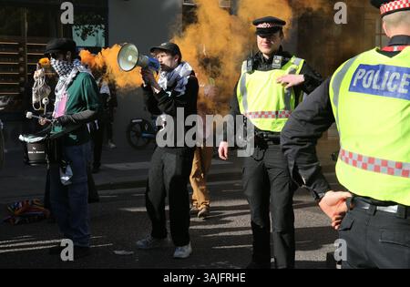 11. April 2025, London, England, Großbritannien: Aktivisten mit Rauchfackeln von Youth Demand blockieren die Kreuzung von Moorgate zum Verkehr in der City of London, während die Polizei anwesend ist. Die Jugendlichen fordern, dass die Unterstützer ihren Monat Straßenschwärmer fortsetzen, um London zum Stillstand zu bringen. Sie blockieren Straßen im Zentrum Londons, um auf die Notlage der palästinensischen Bevölkerung in Gaza und im Westjordanland und die Komplizenschaft der britischen Regierung bei der weiteren Ausfuhr britischer Waffen nach Israel und dem Einsatz von RAF-Anerkennungsflügen über Gaza hinzuweisen. Sie fordern von der britischen Regierung, eine vollständige Rüstungs- und Handelsmasse aufzuerlegen Stockfoto