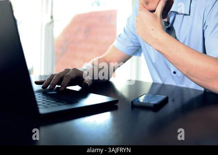 Geschäftsmann sitzt nachdenklich vor dem Laptop, Hand am Kinn Stockfoto
