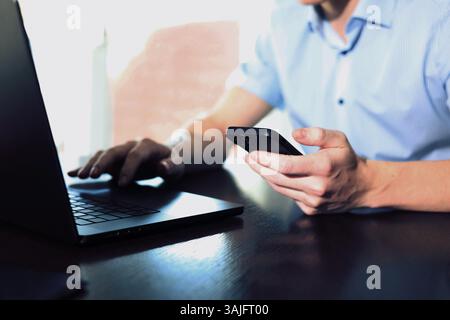 Männlicher Geschäftsmann, der am Laptop arbeitet und das Smartphone in der Hand hält Stockfoto