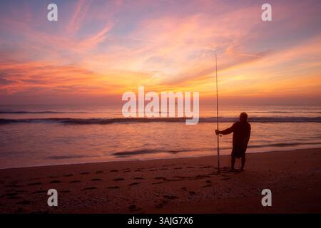 Farbenfroher Sonnenaufgang am Strand mit einem Fischer im Vordergrund Stockfoto