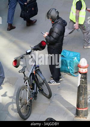 Deliveroo Fahrradfahrer, der vor Bürogebäuden steht, Moorgate, City of London, UK, mit Tasche voller Lebensmittel, die das Mobiltelefon überprüft Stockfoto