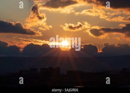Ein atemberaubender Sonnenuntergang mit hellen, glänzenden orangen Farben, die einen warmen, dramatischen und optisch beeindruckenden Abendhimmel schaffen. Stockfoto