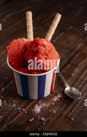 Erdbeereis in gestreifter Tasse mit Waffelrollen auf rustikalem Holz Stockfoto