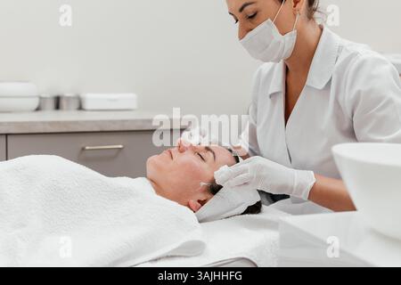 Gesichtsreinigung des weiblichen Gesichtes, Massage, Hautschönheitsbehandlung, entspanntes Mädchen, das professionelle Befeuchtung in der Schönheitsklinik erhält. Werbekonzept Stockfoto