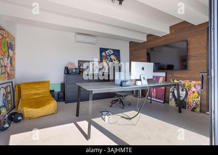 Ein heller und künstlerischer Home Office-Bereich mit auffälliger Graffiti-Kunst, einem modernen schwarzen Schreibtisch und einem iMac-Setup mit Tageslicht. Stockfoto