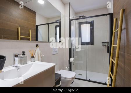 Stilvolles Bad mit großer bodenebener Dusche mit Glastüren, Doppelleitern für Handtücher und warmen Holzakzenten an den Wänden. Stockfoto