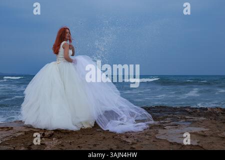 Eine befähigte Frau in einem Hochzeitskleid lässt ihren Freund am Altar und geht an den Strand, Alicante, Spanien Stockfoto