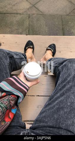 Eine Tasse Kaffee in der Hand, die auf den Stufen in einem Hof sitzt Stockfoto