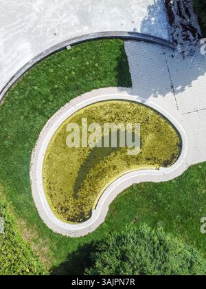 Von oben nach unten geöffnete Sicht auf ein ungepflegtes geometrisches Becken mit verschmutztem Wasser. Stockfoto