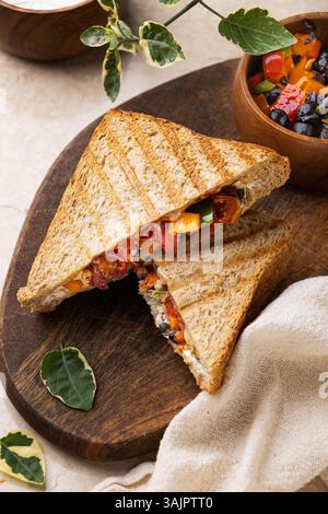 Labneh Sandwich mit Oliven und Paprika auf geröstetem Brot – Lifestyle Shot auf Beige Marmor mit Holzbrett Stockfoto