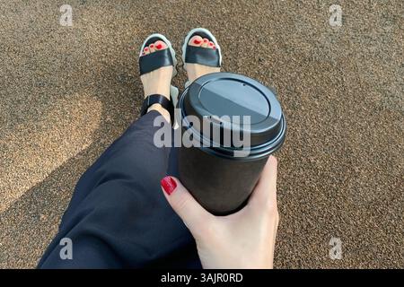 Eine Tasse Kaffee in der Hand, die auf den Stufen in einem Hof sitzt Stockfoto