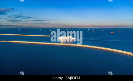 Atemberaubende Aussicht auf die Fähre, die im Sommer 2025 hinter den Wellenbrechern am Eingang zum Hafen von Barcelona vorbeifährt. Stockfoto
