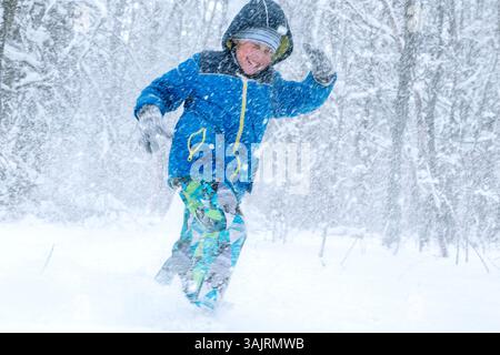 Joyful Child Making Snow Angel in hellblauer Winterjacke Stockfoto