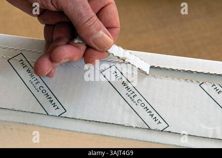 Die Hand eines Mannes öffnet ein Paket, das von der White Company mit ihrem Namen auf einem weißen Karton geschickt wurde. Stockfoto