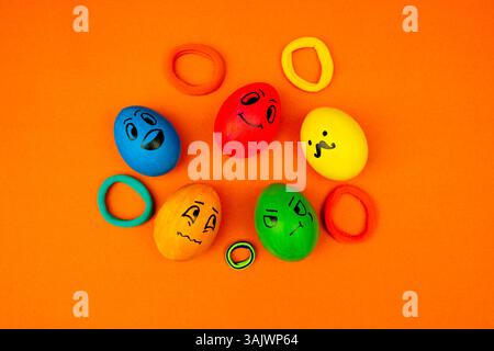 Kreative Ostereier-Gesichter Mit Lustigen Ausdrücken Auf Orange. Fünf bemalte Eier, die auf einem farbenfrohen Set Ausdrücke wie glücklich, verwirrt und wütend zeigen Stockfoto