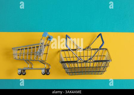 Minimalistisches Einkaufskonzept. Warenkorb und Wagen auf blau-gelbem Hintergrund. Draufsicht Stockfoto