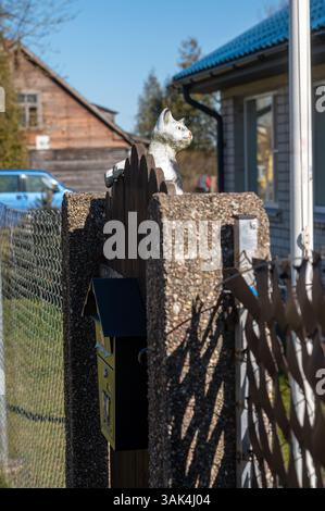 Dekorative Katze auf Holzzaun in der Nähe von charmantem Haus und Briefkasten in ruhiger Landschaft. Stockfoto