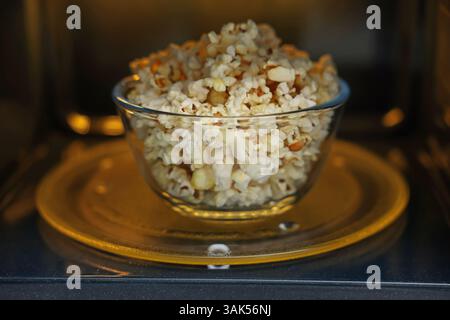 Schüssel mit leckerem Popcorn in der Mikrowelle, Nahaufnahme Stockfoto