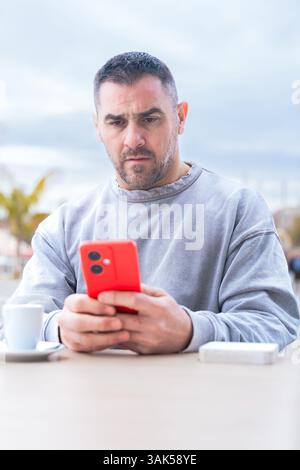 Ernsthafter Mann ernst, während er in einem Café im Freien auf ihrem Smartphone tippt. Vertikal Stockfoto